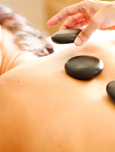 Woman receiving a relaxing hot stone massage with smooth black stones placed on their back.